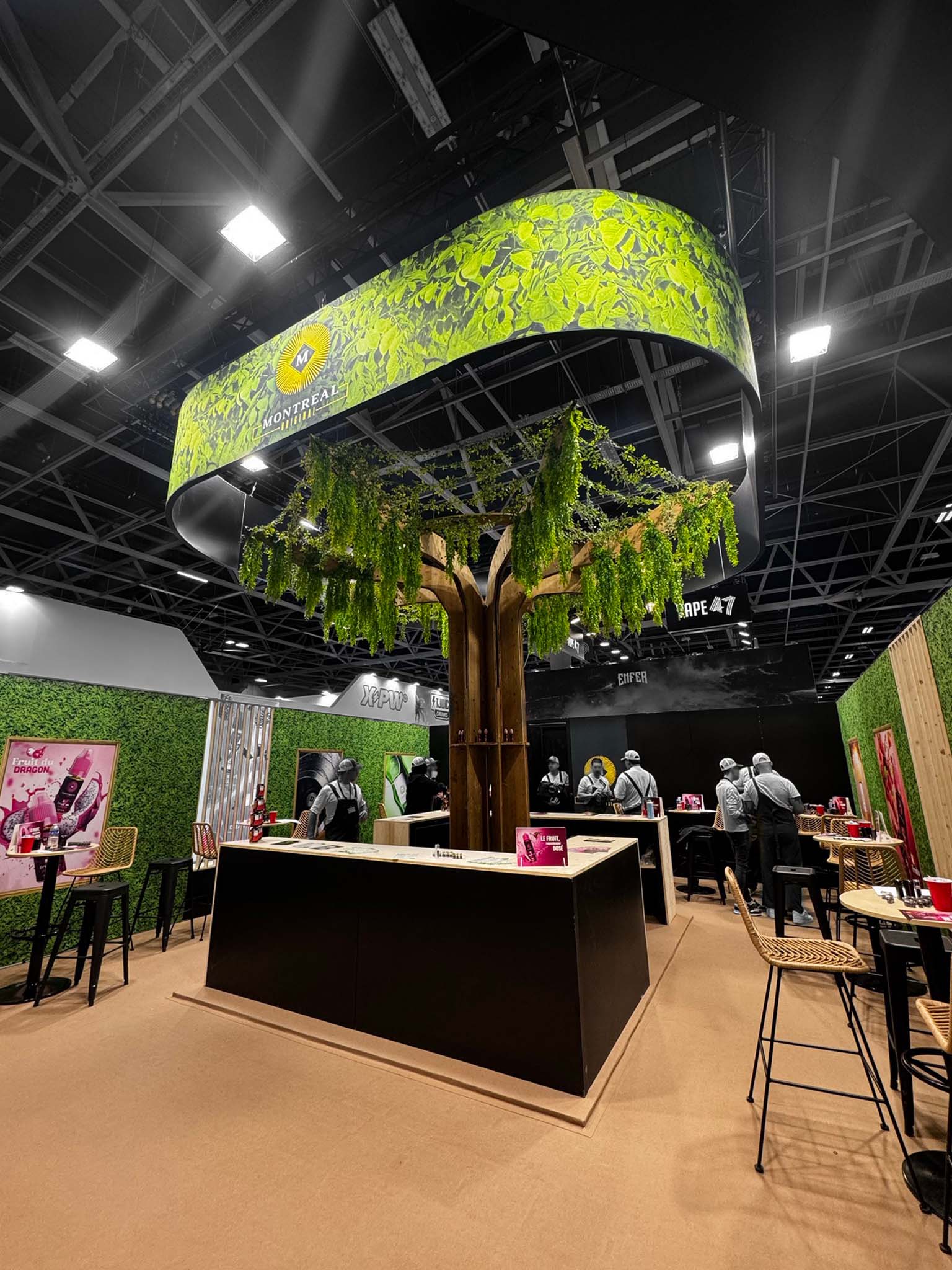 Original Montreal-style green booth design at Vapexpo Paris, featuring a sculpted tree and a hanging sign