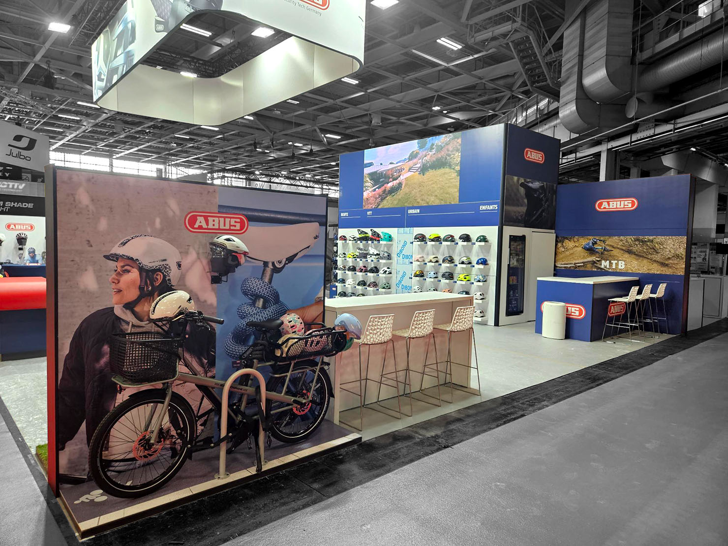 An 80-square-meter ABUS booth at the Prodays trade show in Paris, featuring a wall of helmets and a suspended illuminated sign